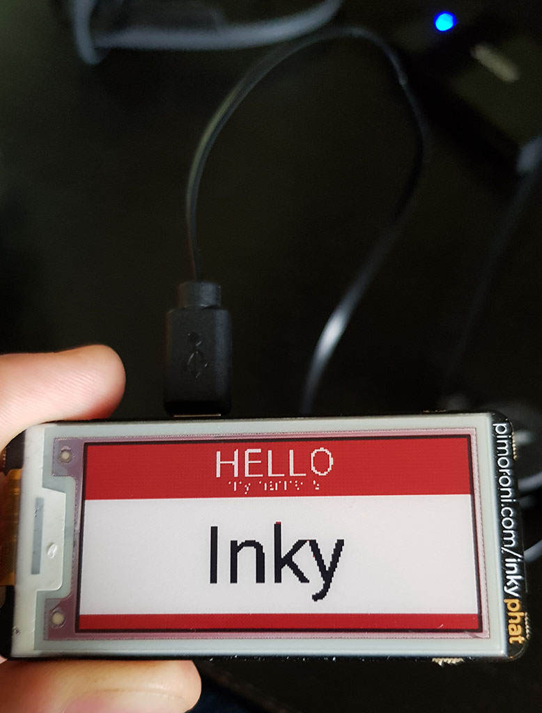 Fingers holding eInk display with text: Hello, my name is Inky